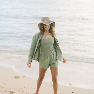 Woman wearing loose button up and smocked tube top with spaghetti straps and short in medium green linen.