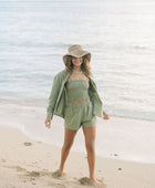 Woman wearing loose button up and smocked tube top with spaghetti straps and short in medium green linen.