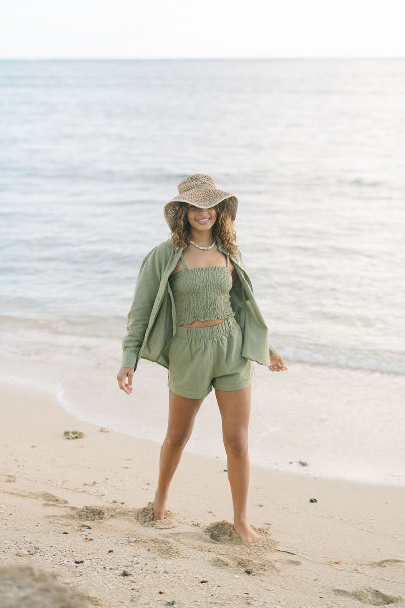 Woman wearing loose button up and smocked tube top with spaghetti straps and short in medium green linen.