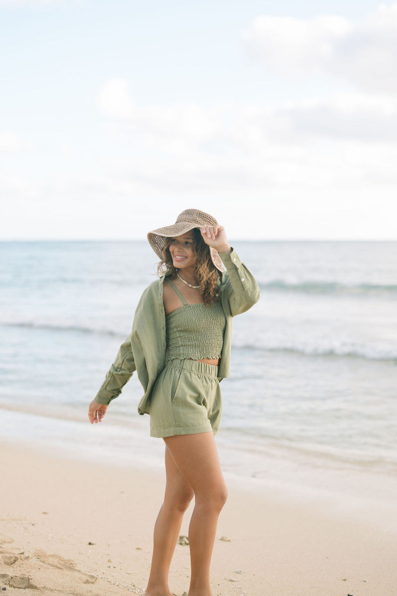 Woman wearing loose button up and smocked tube top with spaghetti straps and short in medium green linen.