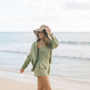 Woman wearing loose button up and smocked tube top with spaghetti straps and short in medium green linen.