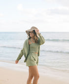 Woman wearing loose button up and smocked tube top with spaghetti straps and short in medium green linen.