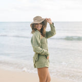Woman wearing loose button up and smocked tube top with spaghetti straps and short in medium green linen.