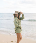 Woman wearing loose button up and smocked tube top with spaghetti straps and short in medium green linen.