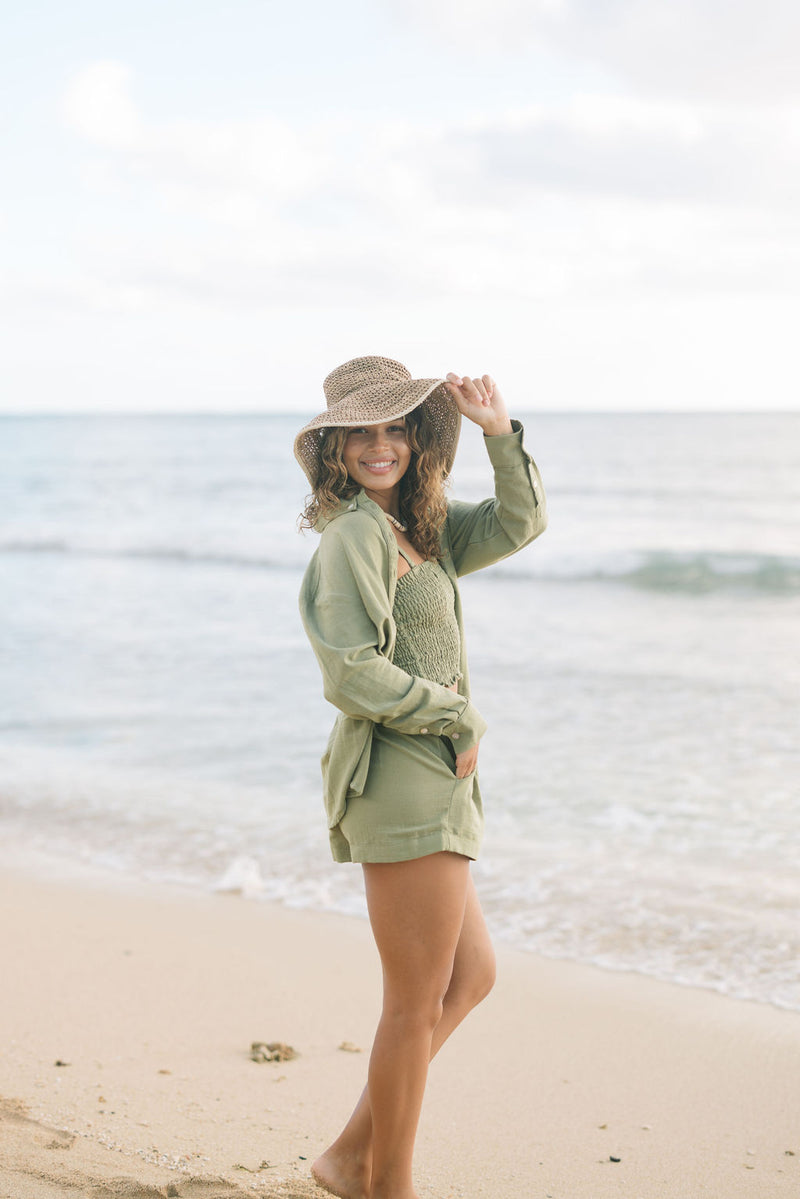 Woman wearing loose button up and smocked tube top with spaghetti straps and short in medium green linen.