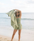 Woman wearing loose button up with smocked tube top and short in medium green linen.