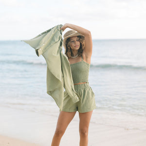 Woman wearing loose button up and smocked tube top with spaghetti straps and short in medium green linen.
