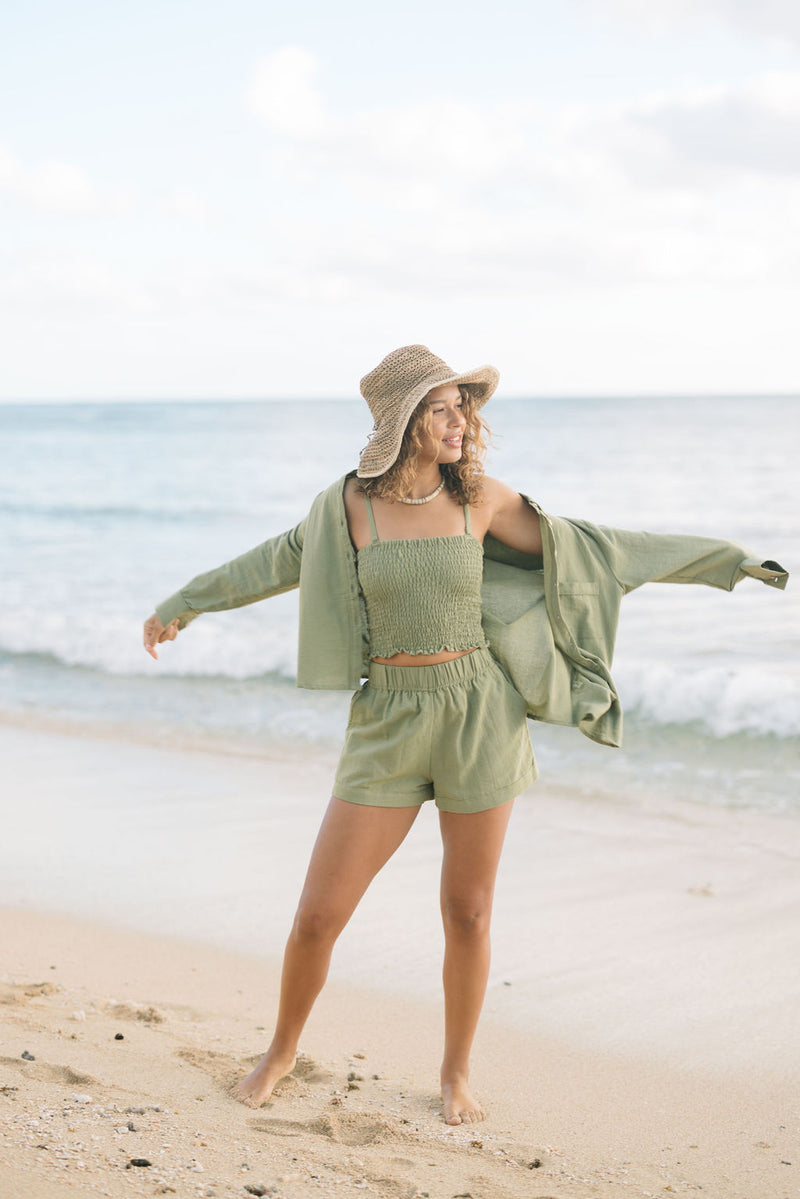 Woman wearing loose button up with smocked tube top and short in medium green linen.