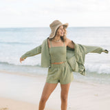 Woman wearing loose button up and smocked tube top with spaghetti straps and short in medium green linen.