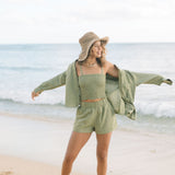 Woman wearing loose button up and smocked tube top with spaghetti straps and short in medium green linen.
