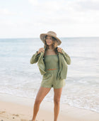 Woman wearing loose button up with smocked tube top and short in medium green linen.