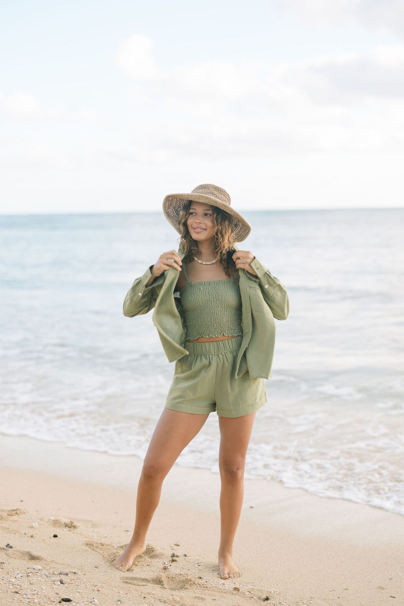 Woman wearing loose button up with smocked tube top and short in medium green linen.