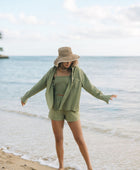 Woman wearing loose button up with smocked tube top and short in medium green linen.