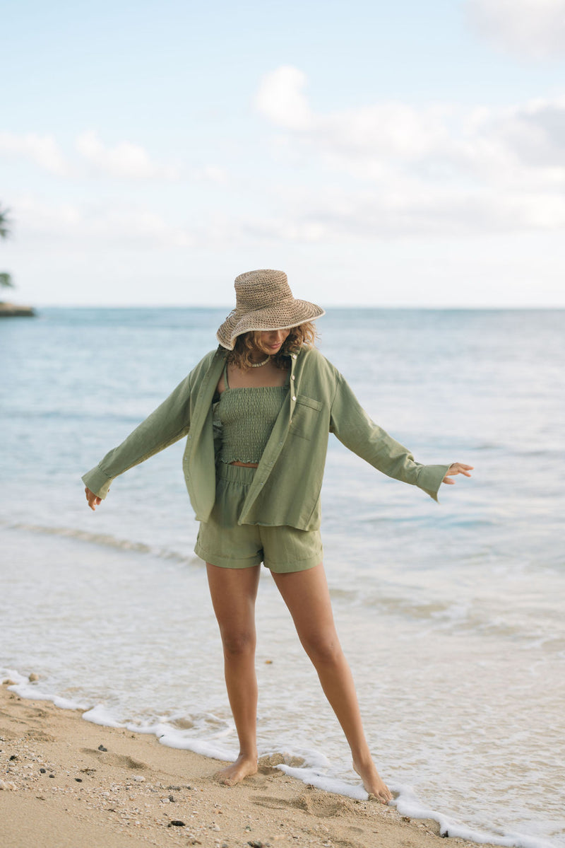 Woman wearing loose button up with smocked tube top and short in medium green linen.