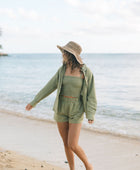 Woman wearing loose button up with smocked tube top and short in medium green linen.