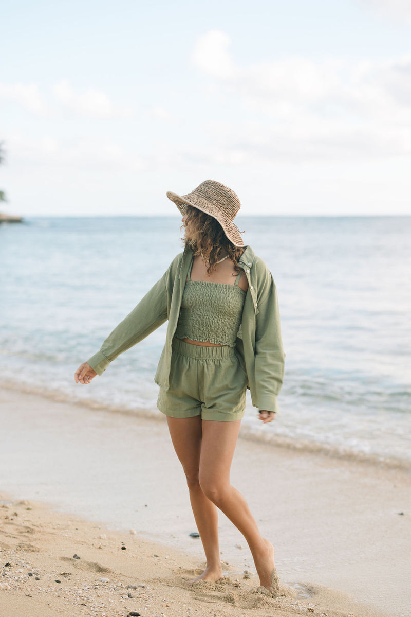 Woman wearing loose button up with smocked tube top and short in medium green linen.