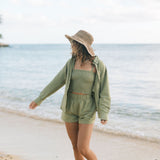 Woman wearing loose button up and smocked tube top with spaghetti straps and short in medium green linen.