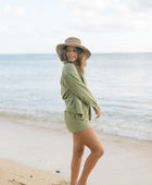 Woman wearing loose button up with smocked tube top and short in medium green linen.