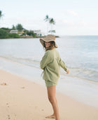 Woman wearing loose button up with smocked tube top and short in medium green linen.