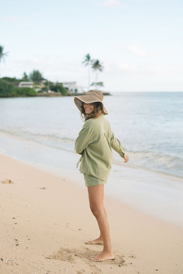 Woman wearing loose button up with smocked tube top and short in medium green linen.