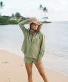 Woman wearing loose button up with smocked tube top and short in medium green linen.