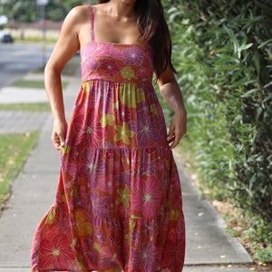 woman wearing terracotta colored tie back dress with large purple and yellow flower print