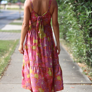 woman wearing terracotta colored tie back dress with large purple and yellow flower print