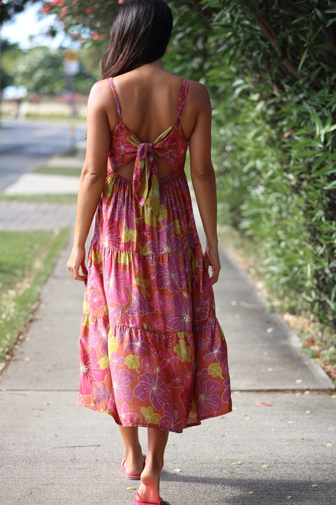 woman wearing terracotta colored tie back dress with large purple and yellow flower print