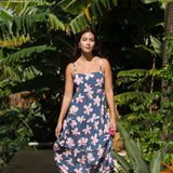 woman with black hair wearing a maxi tiered dress in a navy color with pink hibiscus blossoms 