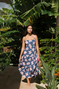 woman with black hair wearing a maxi tiered dress in a navy color with pink hibiscus blossoms 