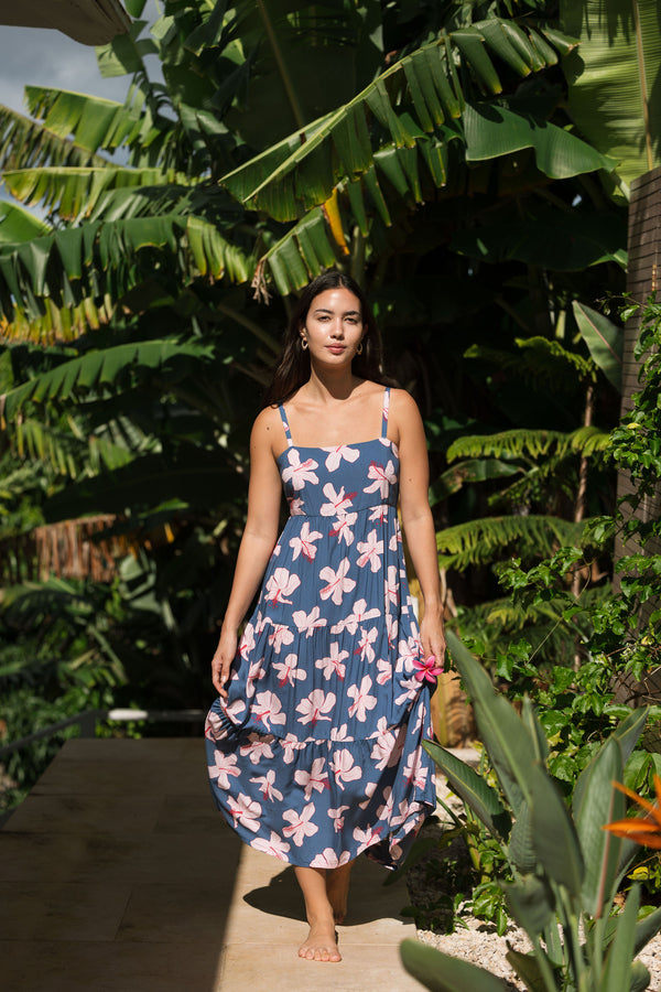 woman with black hair wearing a maxi tiered dress in a navy color with pink hibiscus blossoms 
