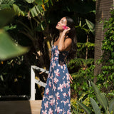 woman with black hair wearing a maxi tiered dress in a navy color with pink hibiscus blossoms 