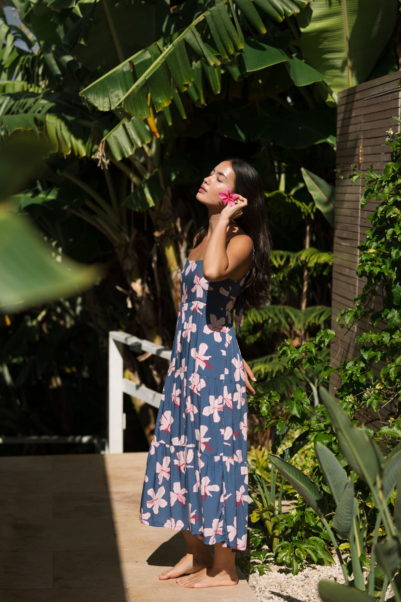woman with black hair wearing a maxi tiered dress in a navy color with pink hibiscus blossoms 