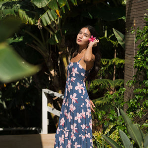 woman with black hair wearing a maxi tiered dress in a navy color with pink hibiscus blossoms 