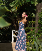 woman with black hair wearing a maxi tiered dress in a navy color with pink hibiscus blossoms 