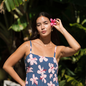 woman with black hair wearing a maxi tiered dress in a navy color with pink hibiscus blossoms 