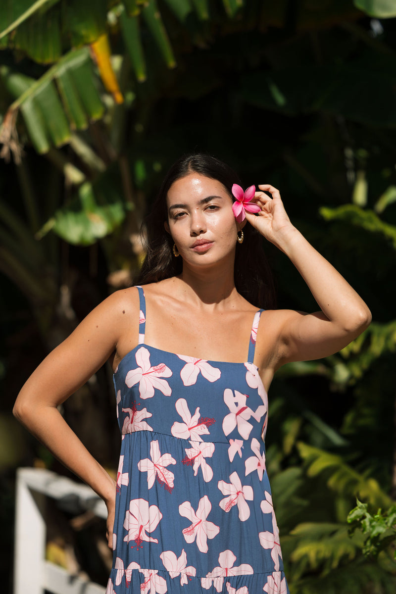 woman with black hair wearing a maxi tiered dress in a navy color with pink hibiscus blossoms 