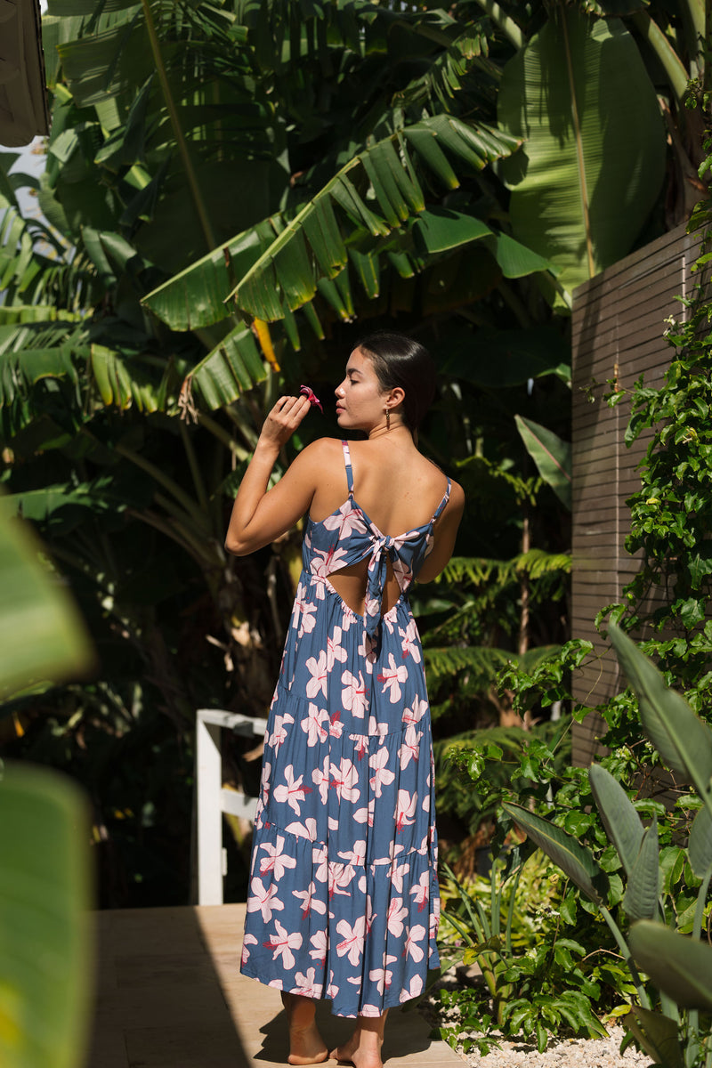 woman with black hair wearing a maxi tiered dress in a navy color with pink hibiscus blossoms 