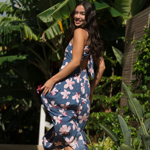 woman with black hair wearing a maxi tiered dress in a navy color with pink hibiscus blossoms 
