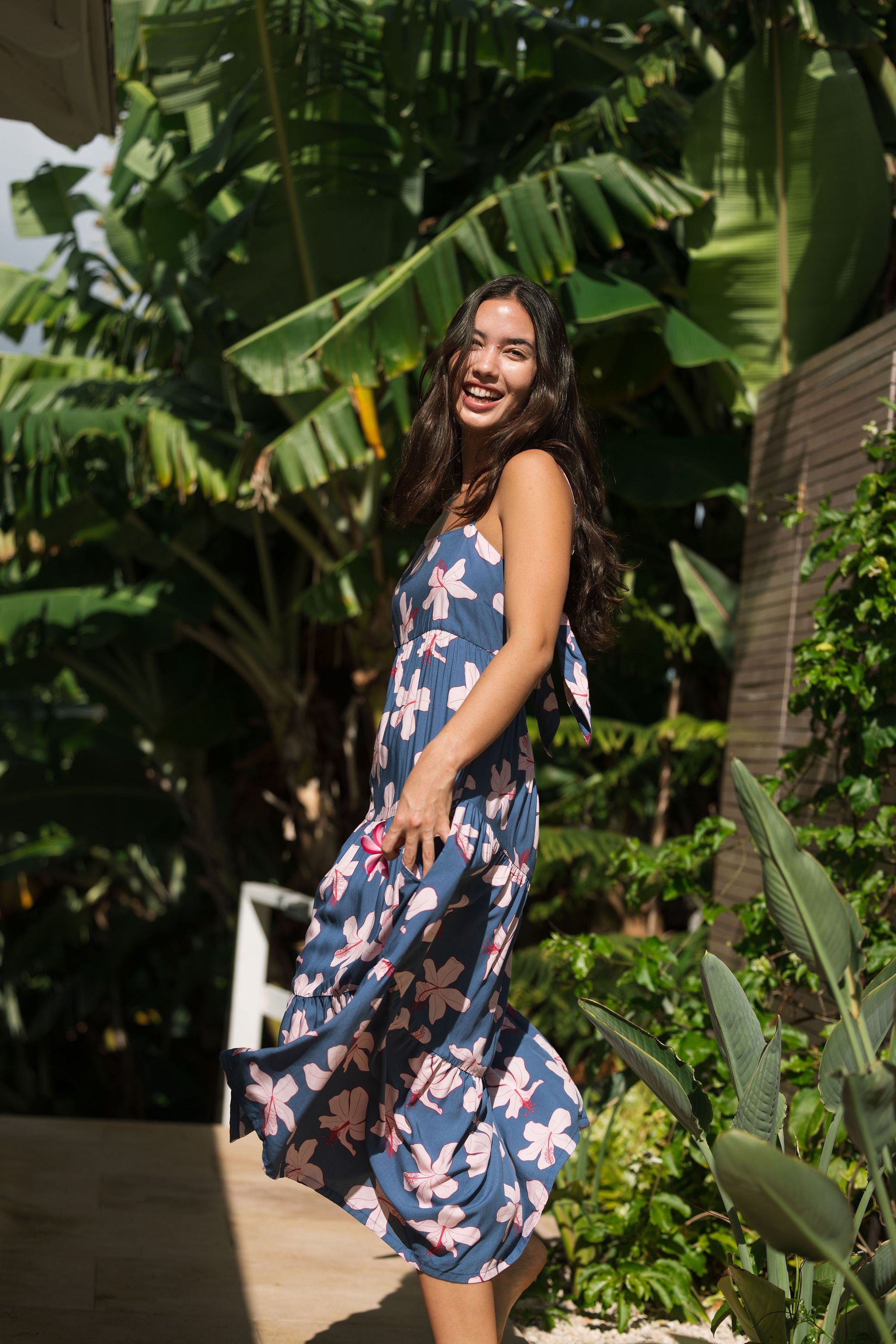 woman with black hair wearing a maxi tiered dress in a navy color with pink hibiscus blossoms 