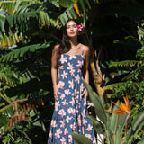 woman with black hair wearing a maxi tiered dress in a navy color with pink hibiscus blossoms 