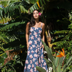 woman with black hair wearing a maxi tiered dress in a navy color with pink hibiscus blossoms 