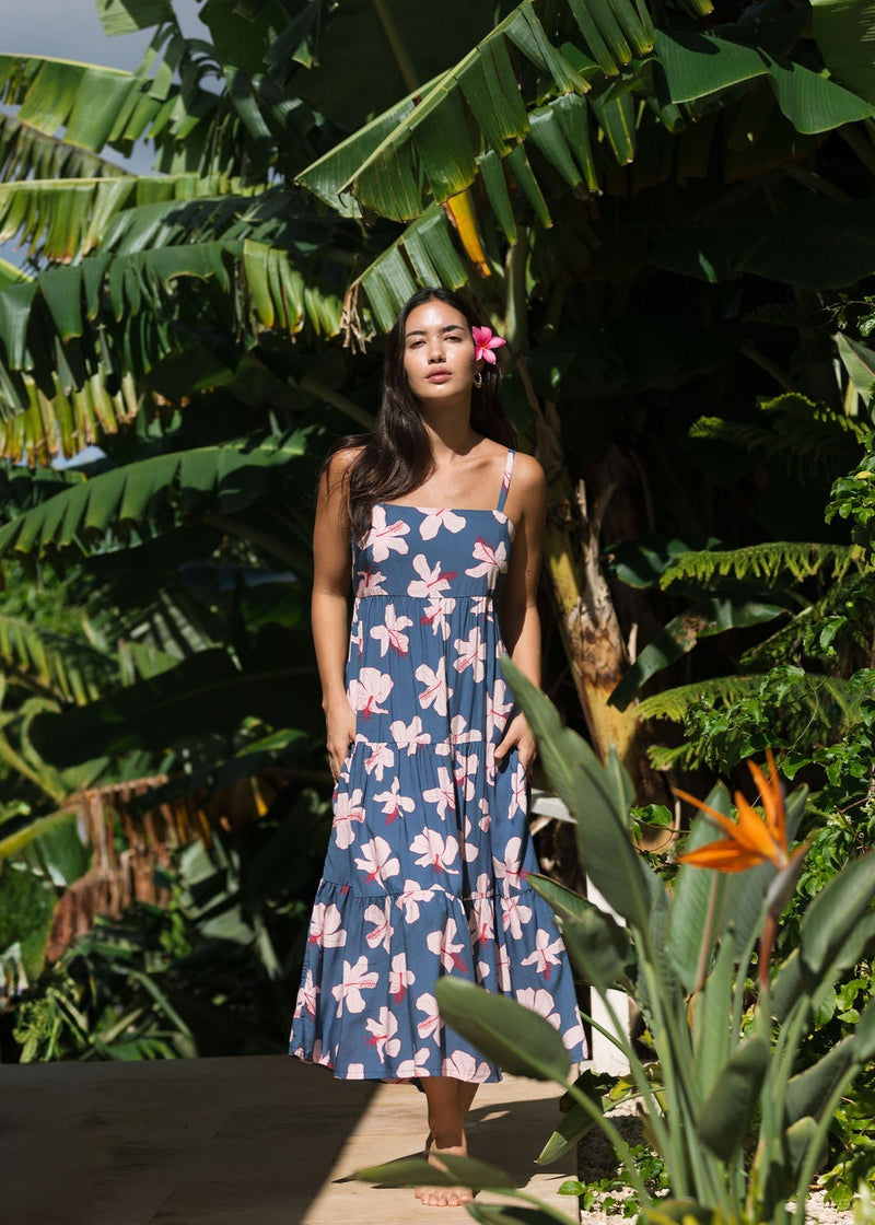 woman with black hair wearing a maxi tiered dress in a navy color with pink hibiscus blossoms 