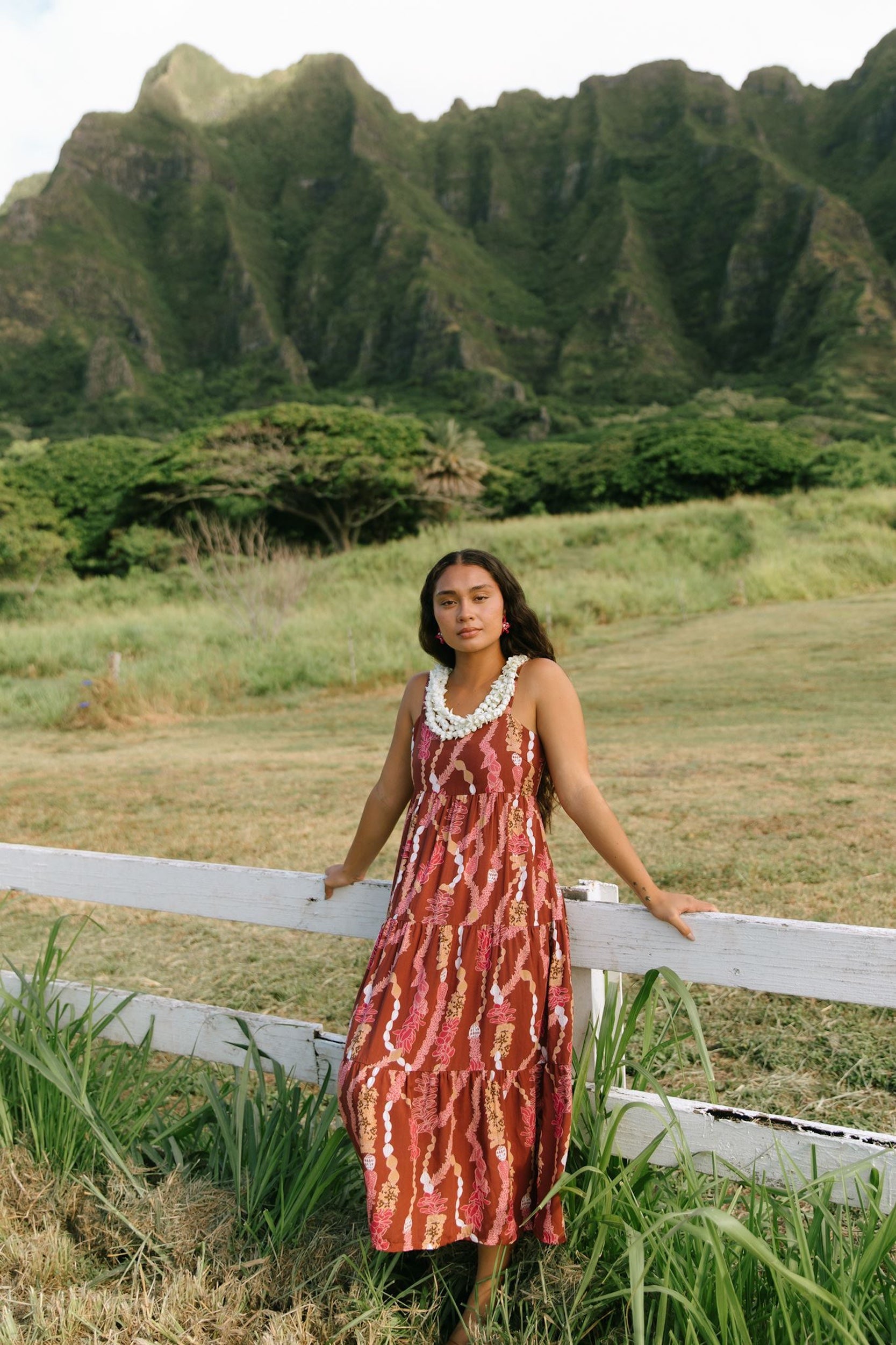 woman with brown hair wearing red-brown maxi dress with lei print