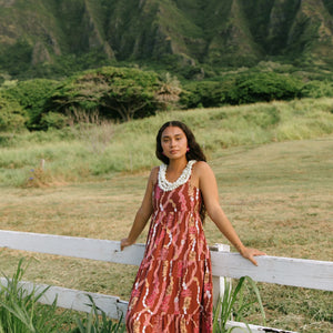 woman with brown hair wearing red-brown maxi dress with lei print