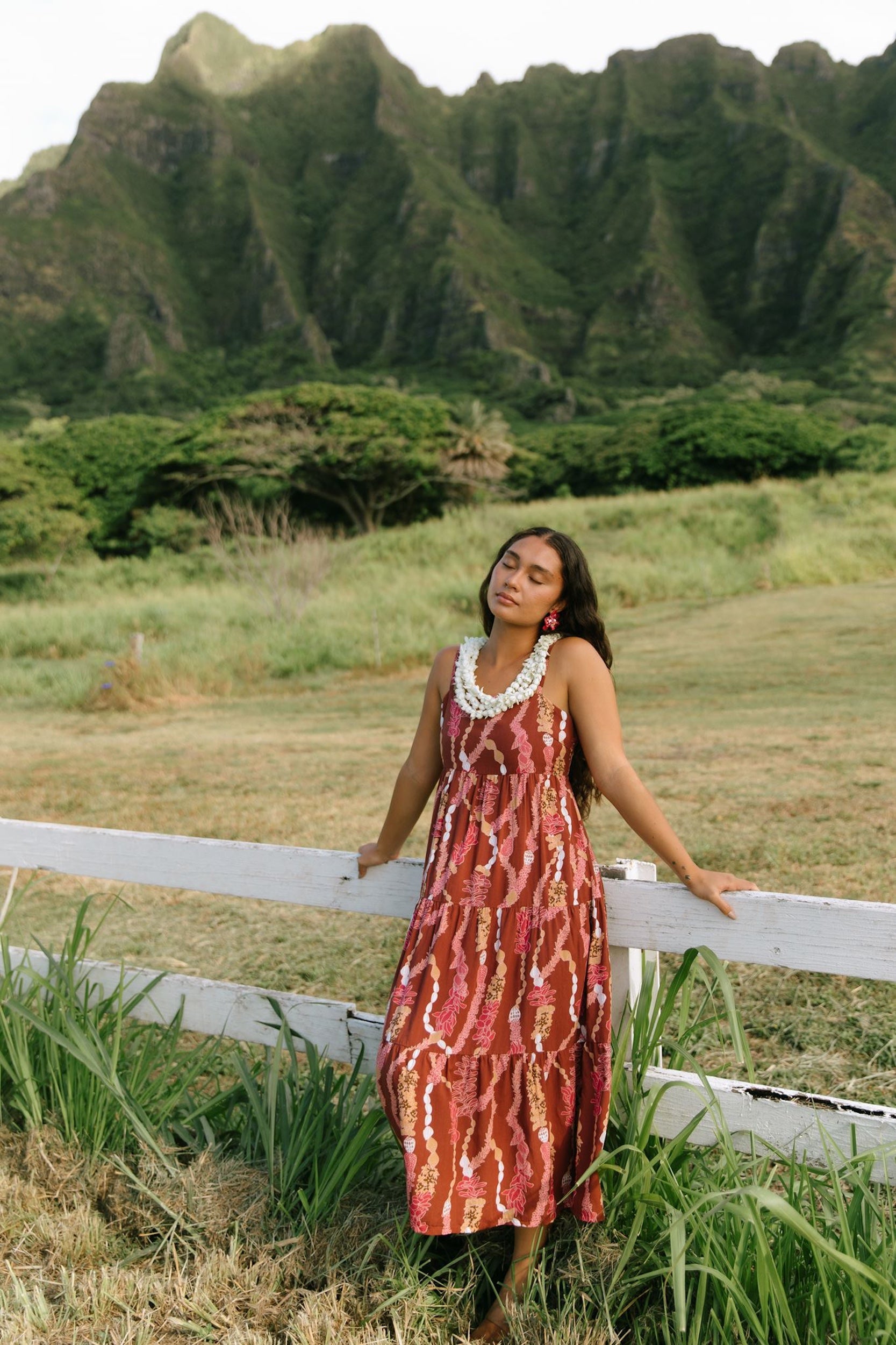 woman with brown hair wearing red-brown maxi dress with lei print