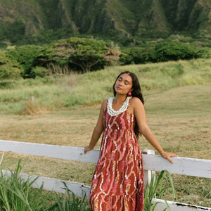 woman with brown hair wearing red-brown maxi dress with lei print