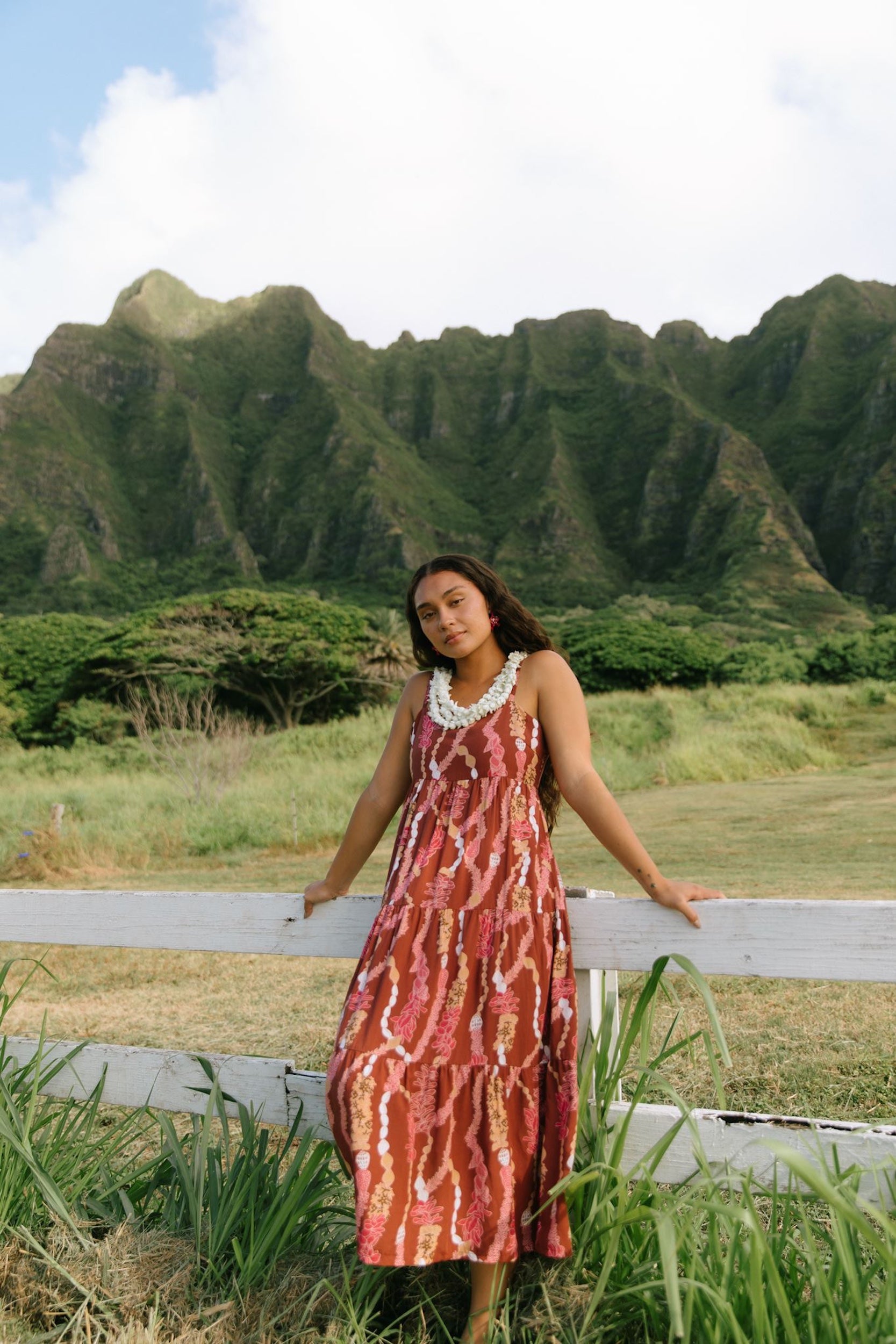 woman with brown hair wearing red-brown maxi dress with lei print