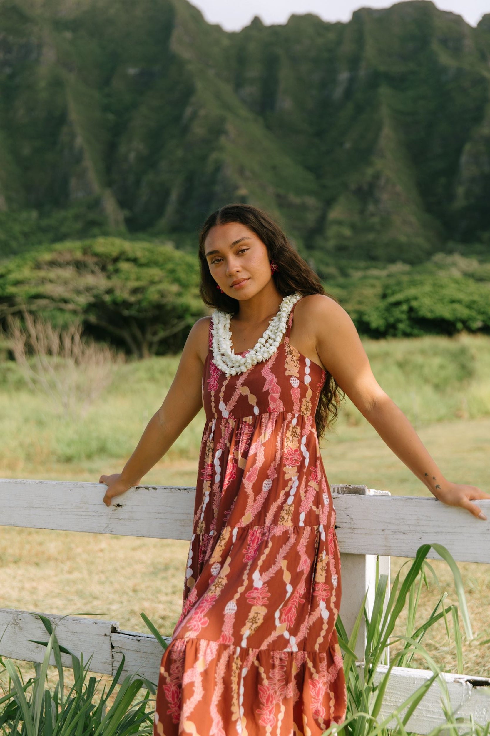woman with brown hair wearing red-brown maxi dress with lei print
