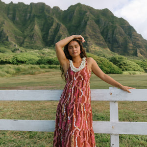 woman with brown hair wearing red-brown maxi dress with lei print